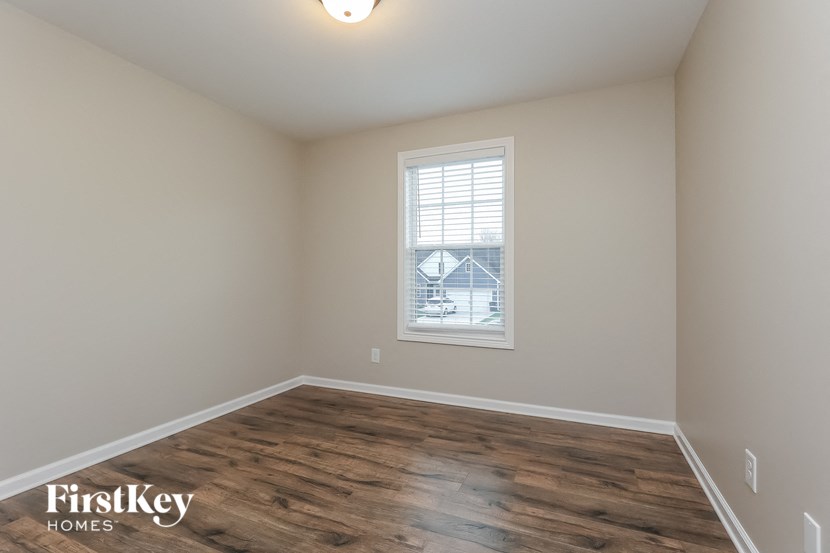 A room with wooden flooring and a window showing a house in the distance.