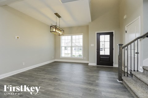 A spacious room with a wooden floor and a staircase on the right side.
