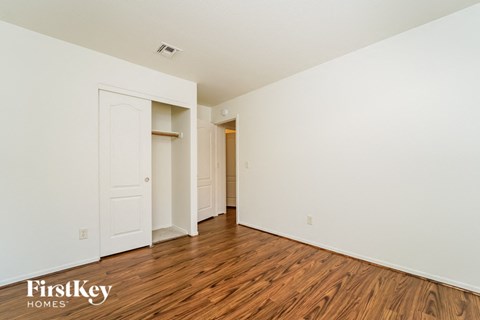 a bedroom with white walls and wood flooring and a closet