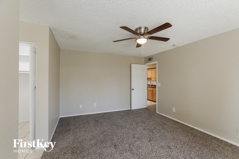 an empty living room with a ceiling fan and a door to a kitchen