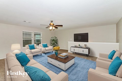 A living room with a blue rug and a ceiling fan.