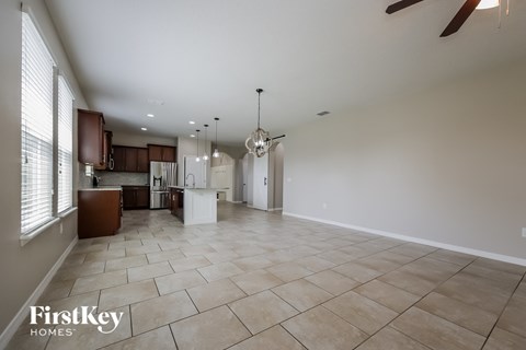 A spacious living room with a kitchen in the background and a fan hanging from the ceiling.