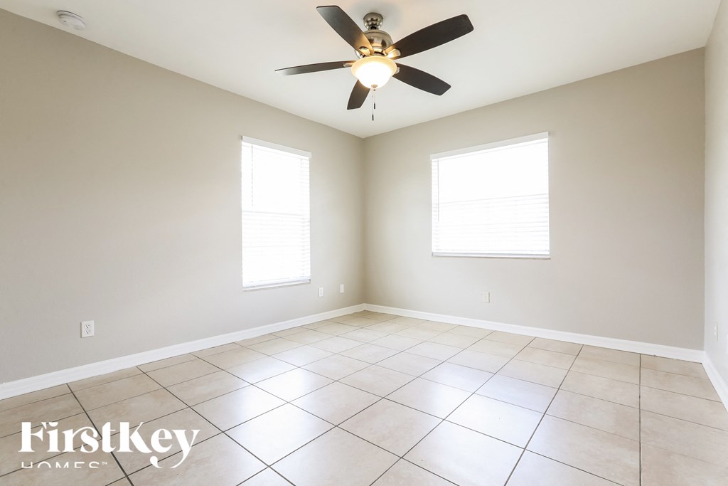 an empty living room with a ceiling fan and two windows