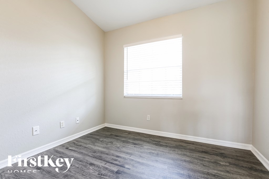 a bedroom with white walls and wood floors and a window