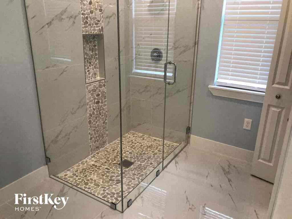 A shower with a glass door and a marble floor.
