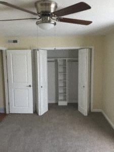 A room with a ceiling fan and a closet with shelves.
