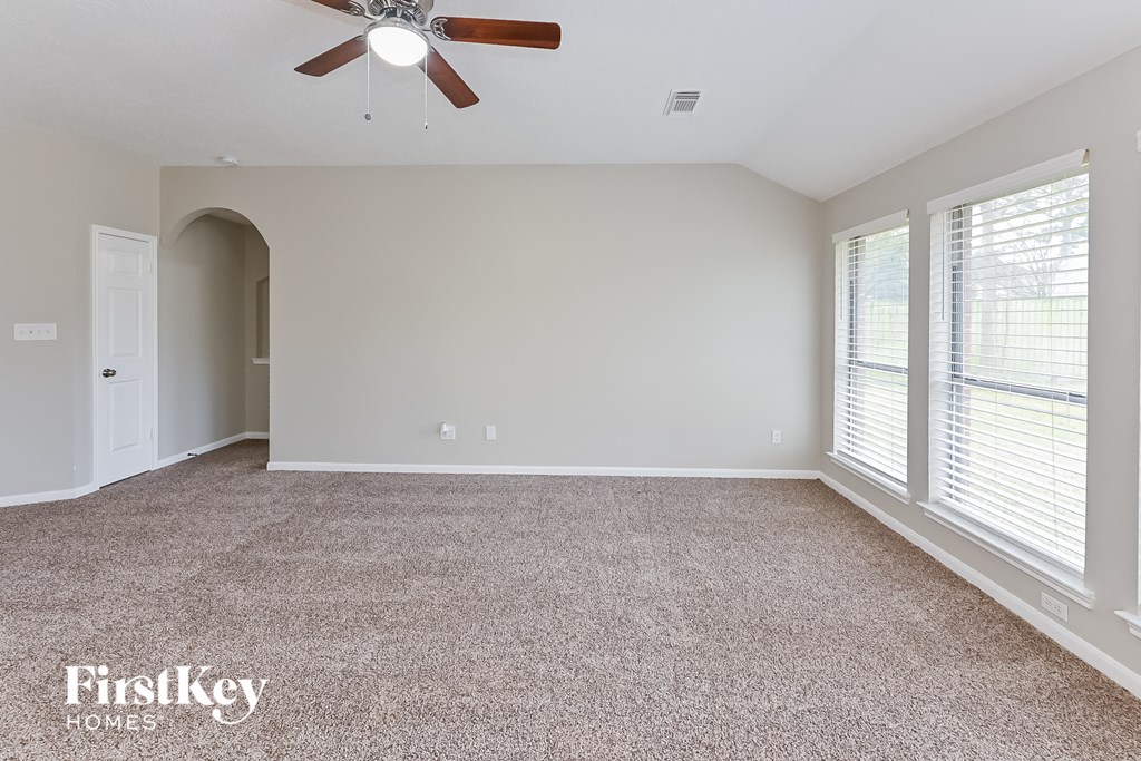 an empty living room with a ceiling fan and large windows