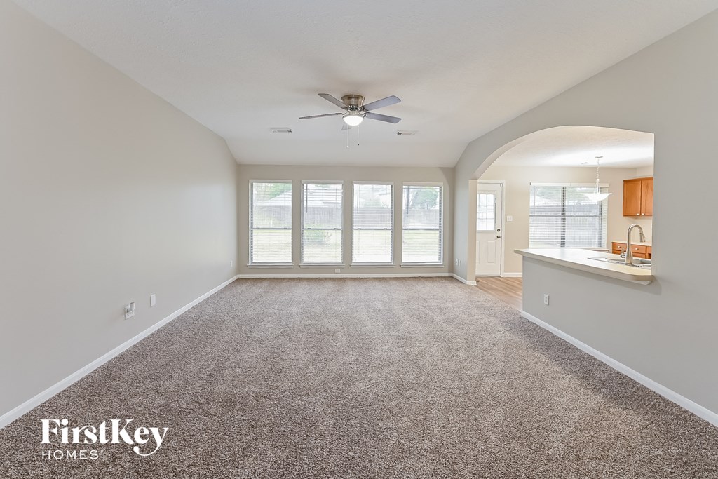 an empty living room with a ceiling fan and a kitchen