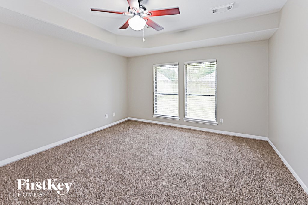an empty living room with a ceiling fan and two windows