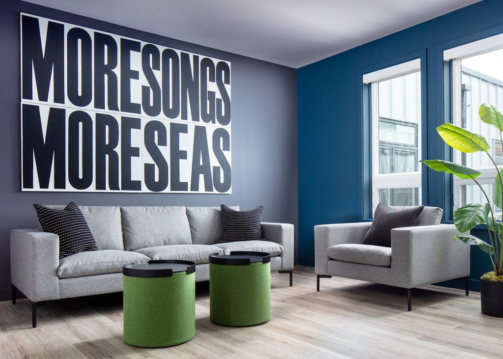 A living room with a grey couch, two green stools and a wall with the words