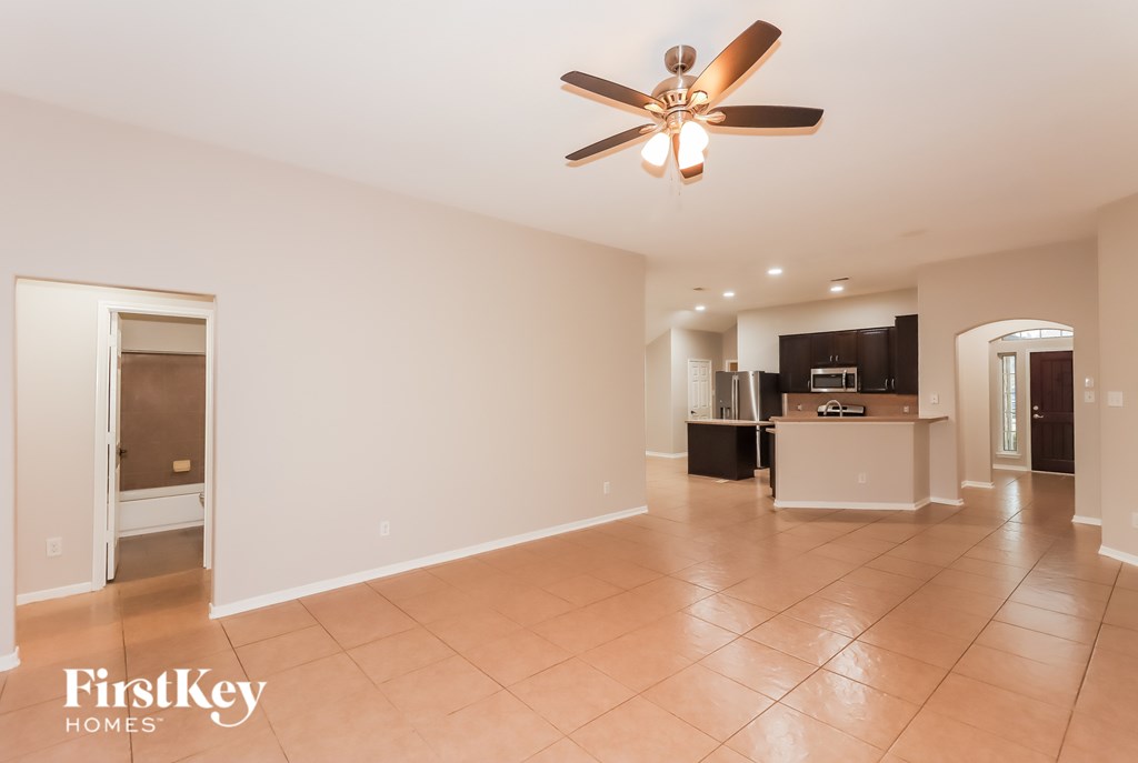 A spacious room with a ceiling fan and a kitchen area in the background.