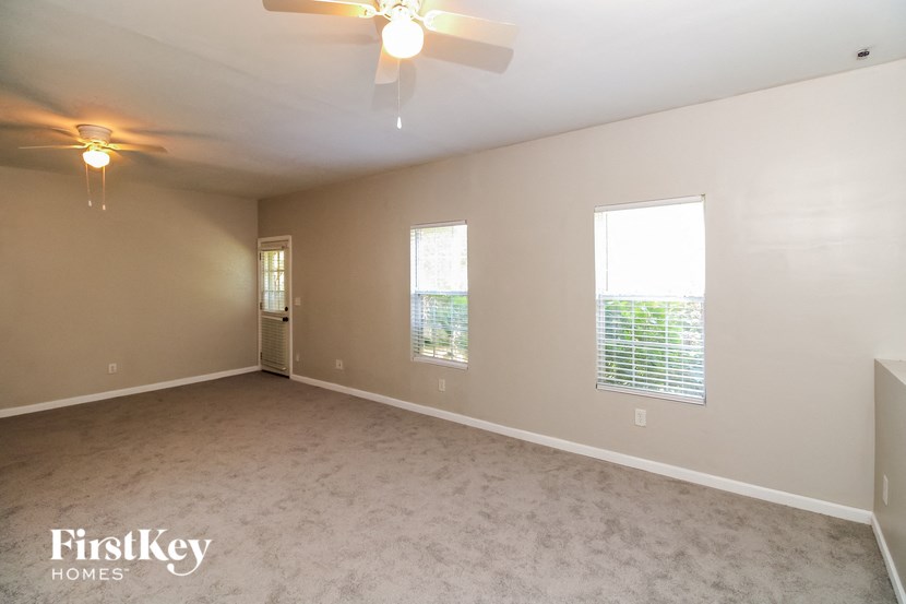 an empty living room with a ceiling fan and two windows