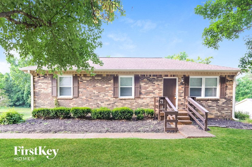 A brick house with a porch and a tree in front.