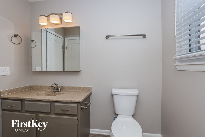 A bathroom with a toilet, sink, mirror, and a towel bar.