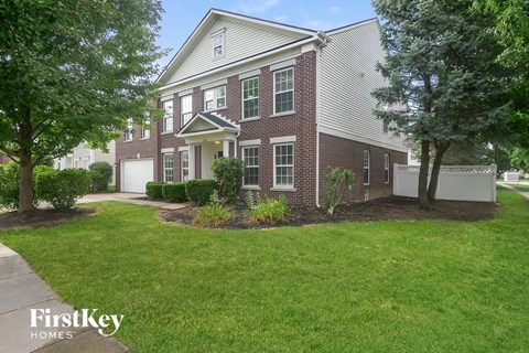A brick house with a white garage door and a tree in front.