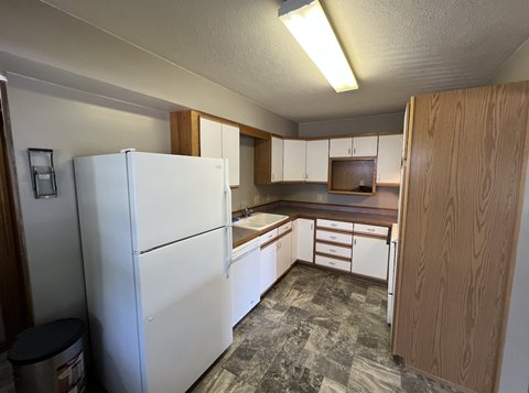 A kitchen with a white refrigerator, wooden cabinets, and a tiled floor.