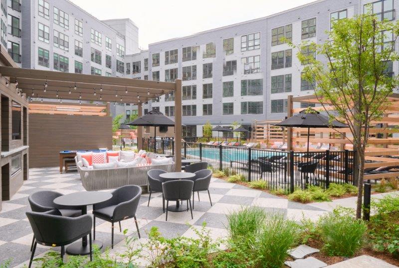 a patio with tables and chairs and a pool in front of a building