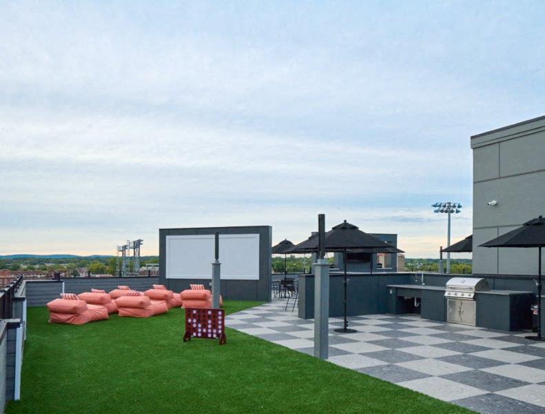 the roof terrace of the building has a lawn and chairs and a movie theater