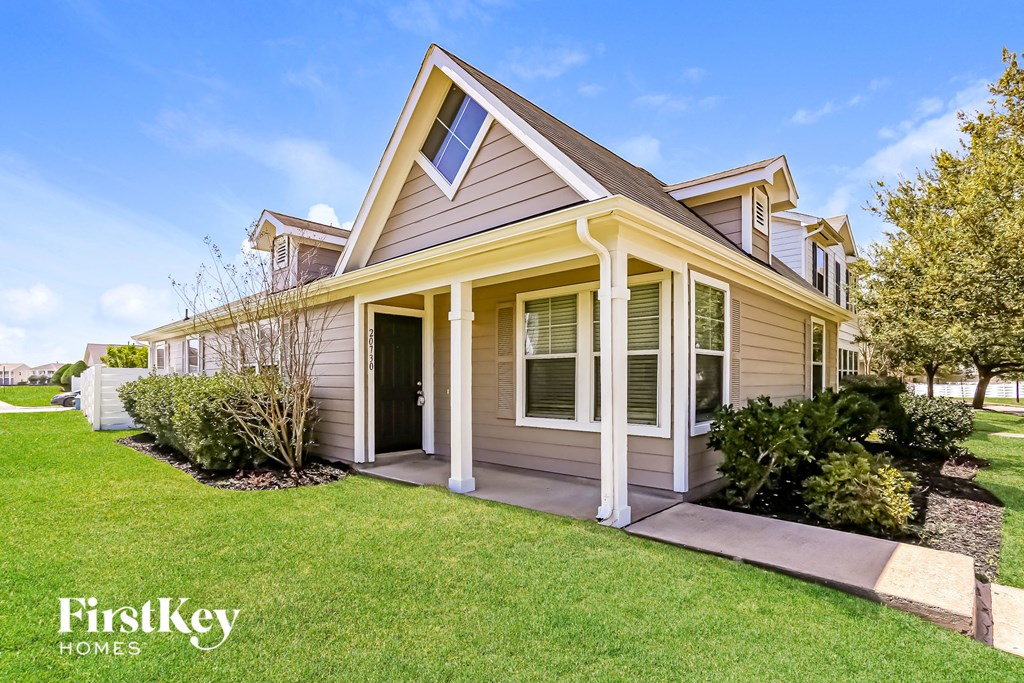 a tan house with a porch and a lawn