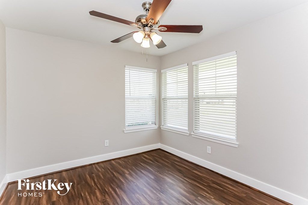 an empty room with a ceiling fan and three windows