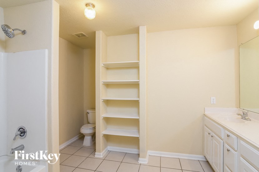 A white bathroom with a toilet, sink, and shelves.