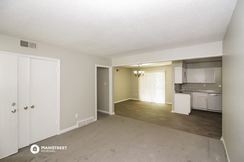 an empty living room and kitchen with white cabinets and appliances