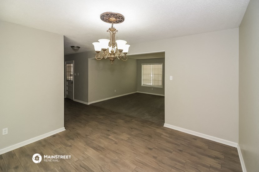 an empty living room with a chandelier and wood flooring