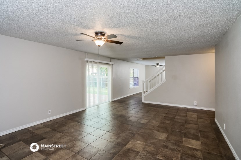 an empty living room with a ceiling fan and a staircase