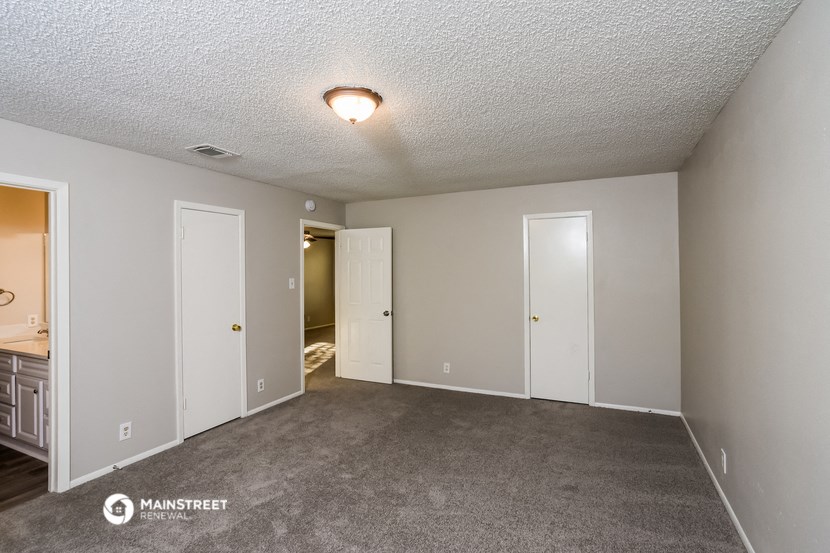 the living room of an apartment with carpet and a door to the bathroom