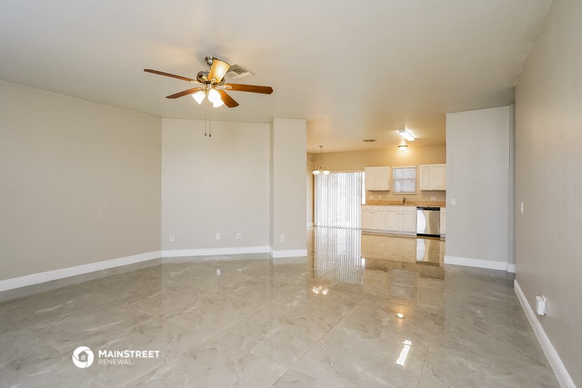an empty living room with a ceiling fan and a kitchen