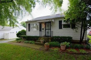 A small white house with a black door and windows surrounded by a green lawn.
