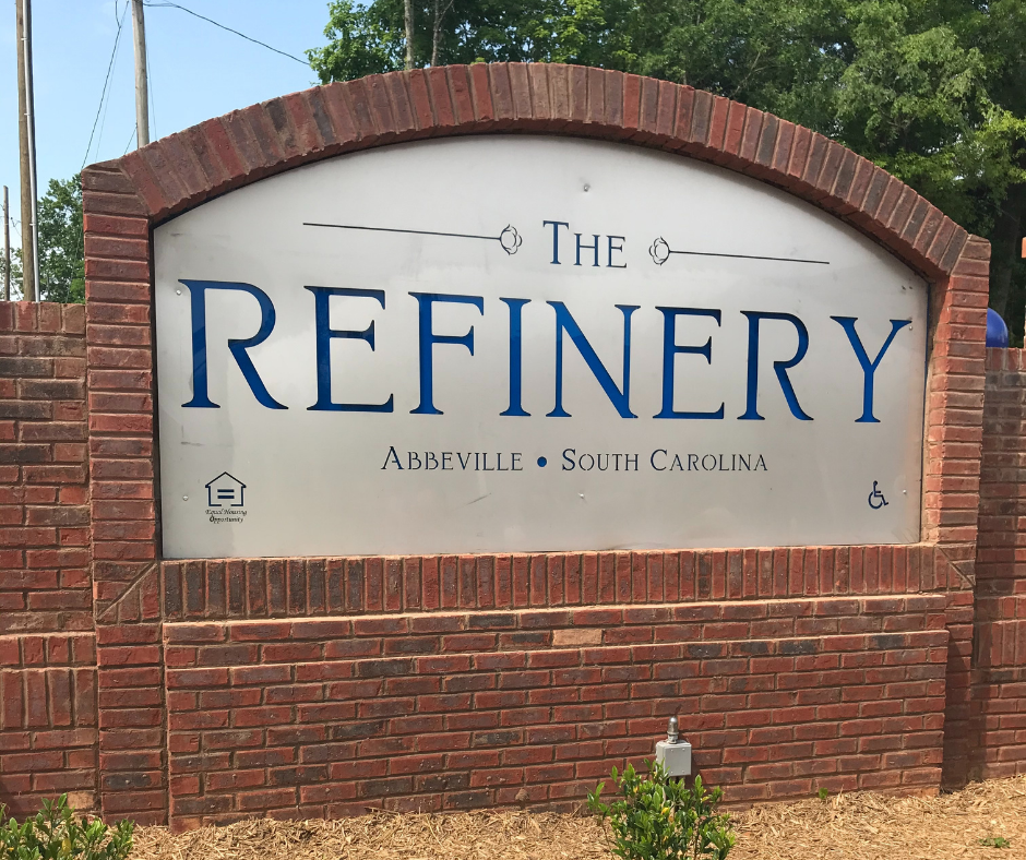 A sign that says "The Refinery" in blue letters on a brick wall.