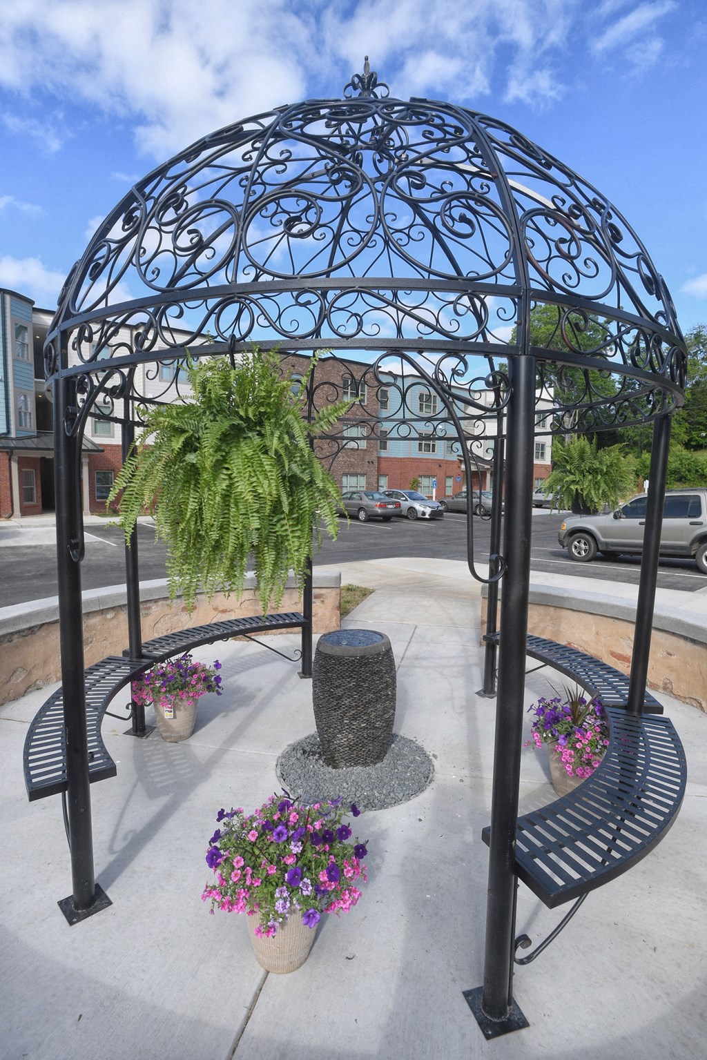 A black wrought iron gazebo with a cactus plant and purple flowers in front of a building.