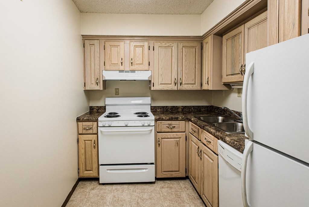 A kitchen with a white refrigerator, white stove, and wooden cabinets.