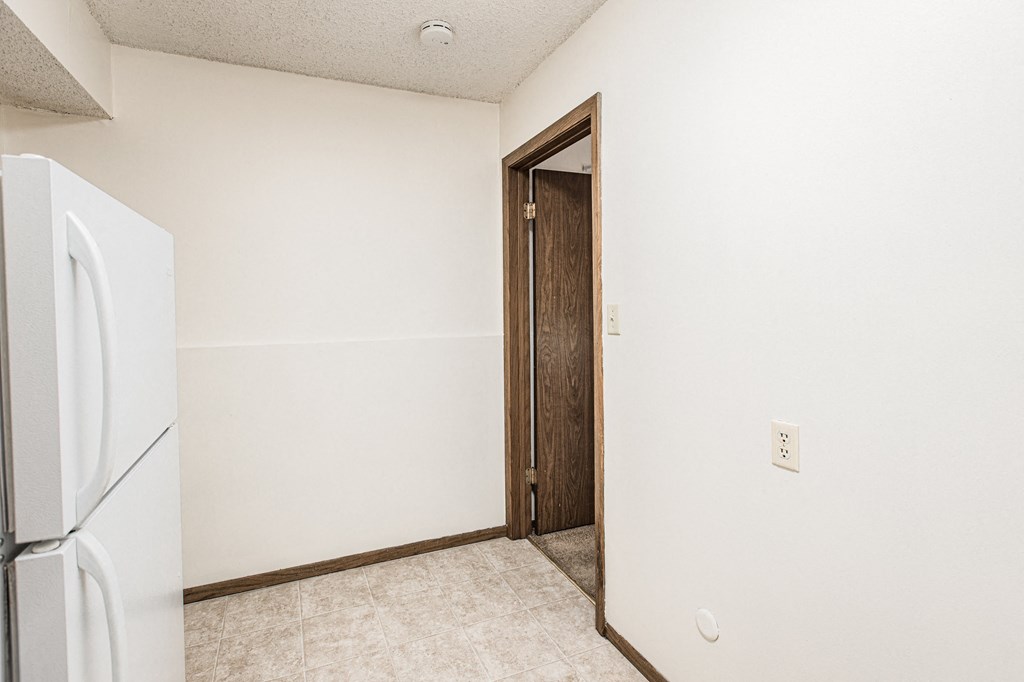A white refrigerator sits in a kitchen next to a wooden door.