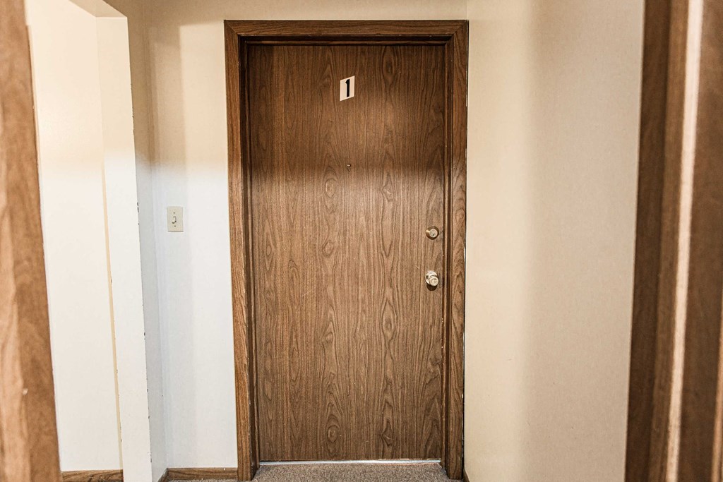 A brown door with a silver handle is in a white hallway.