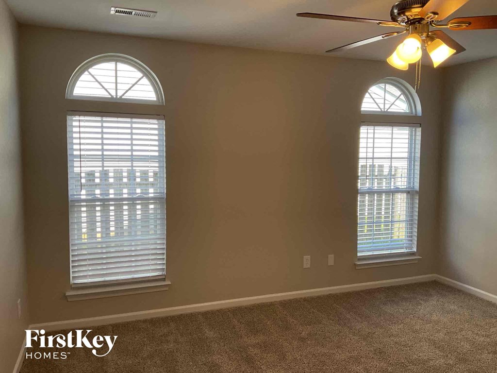 an empty living room with two windows and a ceiling fan