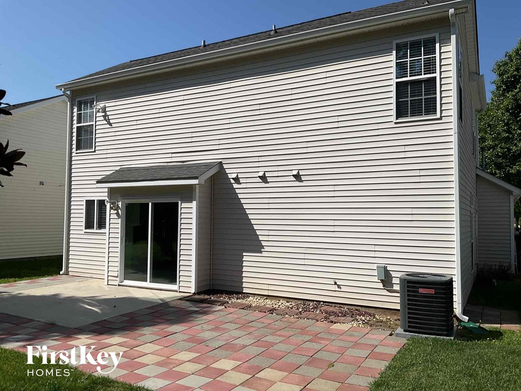 a side view of a white house with a driveway and a trash can