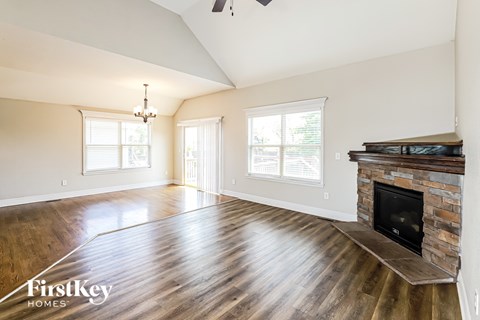 A spacious living room with wood flooring and a stone fireplace.