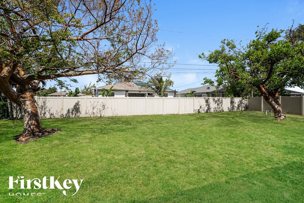 a backyard with grass and trees and a white fence
