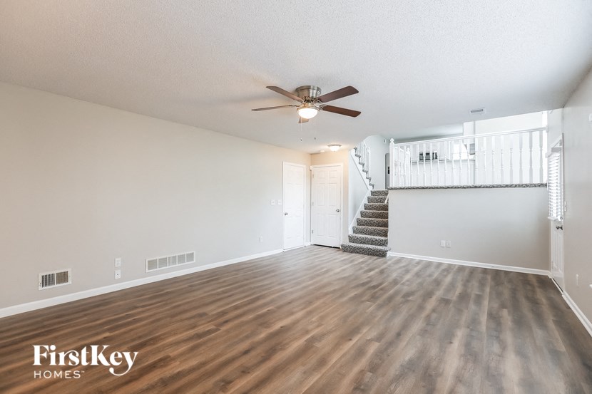an empty living room with a ceiling fan and a staircase