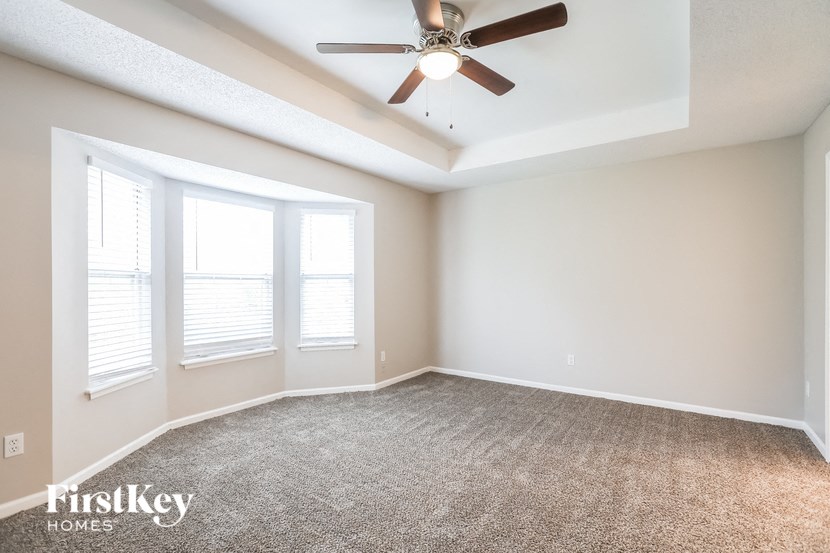 an empty living room with a ceiling fan and three windows