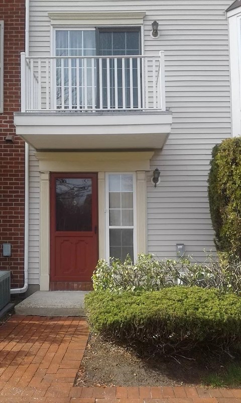 A red door is on the left side of a grey house.