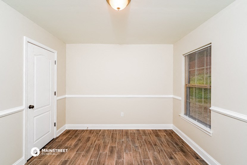 the living room of an empty home with wood flooring and a window