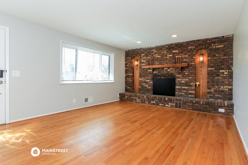 an empty living room with a brick fireplace and wooden floors