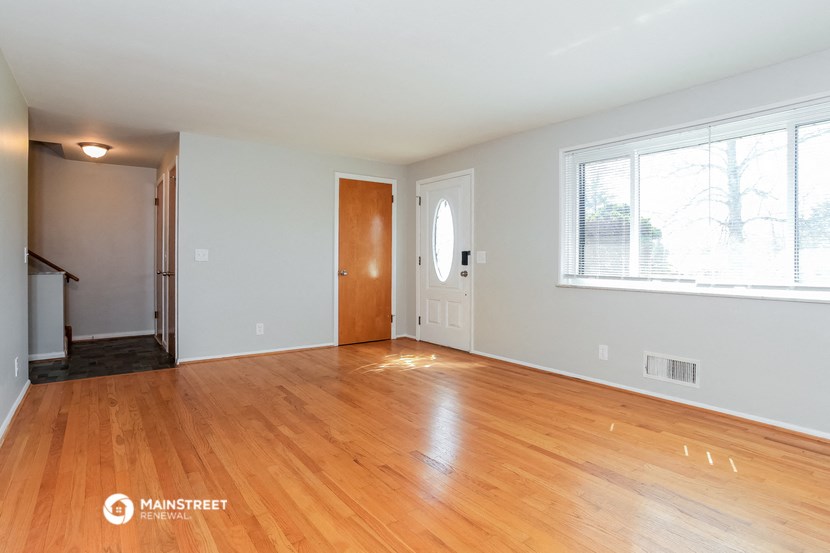 an empty living room with wood flooring and a door to a hallway