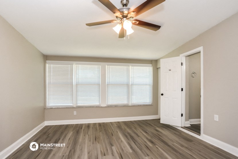 the spacious living room with large windows and a ceiling fan