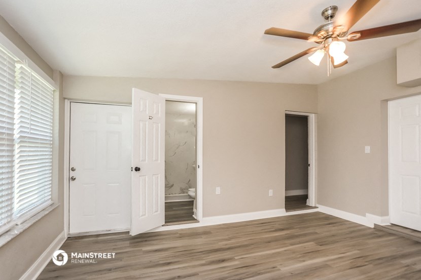 an empty living room with a ceiling fan and a door to a bathroom