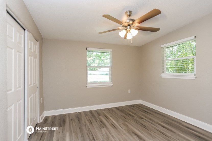an empty room with a ceiling fan and two windows