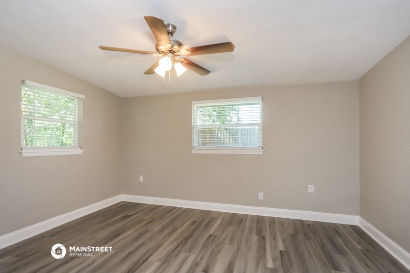 the spacious living room with hardwood floors and a ceiling fan